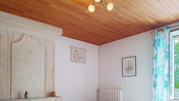 A room with a wooden ceiling, a white radiator, a wooden chair, and two framed artworks on the wall. - Le Village by Interhome (Meuvaines)