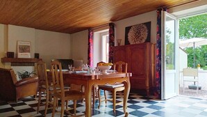 A dining area with a wooden table and chairs, a checkered floor, a radiator, and a view through an open door to an outdoor patio. - Le Village by Interhome (Meuvaines)