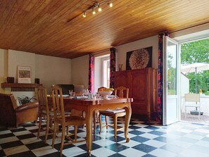 A dining area with a wooden table and chairs, a checkered floor, a radiator, and a view through an open door to an outdoor patio. - Le Village by Interhome (Meuvaines)
