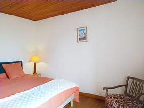 A bedroom with a bed, a chair, a lamp, and a framed picture on the wall. - Le Village by Interhome (Meuvaines)
