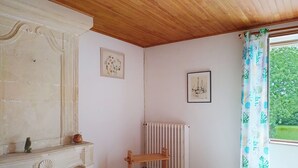 A room with a wooden ceiling, a radiator, a wooden chair, a fireplace, and a window with a curtain. - Le Village by Interhome (Meuvaines)