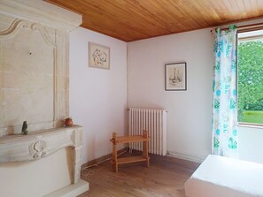 A room with a wooden ceiling, a radiator, a wooden chair, a fireplace, and a window with a curtain. - Le Village by Interhome (Meuvaines)