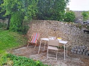 A stone wall, a striped chair, a white table, and a bowl of fruit. - Le Village by Interhome (Meuvaines)