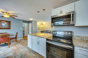 Una cocina con armarios blancos, encimera de granito, estufa de acero inoxidable y ventilador de techo.