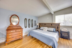 A bedroom with a wooden dresser, a bed with a blue and white striped bedspread, a wooden headboard, a wall-mounted mirror, and a wood-burning stove. - Couples Outdoor Retreat Near Garden of the Gods (Colorado Springs)