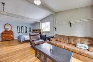 A spacious living room with a large brown leather sofa, a wooden coffee table, a wooden dresser, and a bed with a blue bedspread. - Couples Outdoor Retreat Near Garden of the Gods (Colorado Springs)