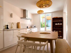 A modern kitchen with white cabinetry, a wooden dining table, and a hanging light fixture. - Calanca - Niolon - Renovated, sea view, 1 min walk (Le Rove)