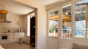 Une cuisine moderne dotée d’appareils électroménagers intégrés, un coin repas avec une table ronde en bois et une vue sur un balcon aménagé avec du mobilier d’extérieur.