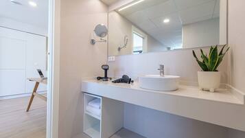 Un baño moderno con tocador blanco, espejo redondo, lavamanos y planta en maceta.