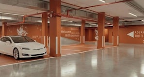 A white car parked in a modern, spacious parking garage with orange accents and multilingual welcome signs.