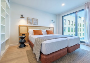 Un dormitorio moderno con una cama grande, una mesita de noche, una lámpara de pared y un ventanal con vistas a edificios.