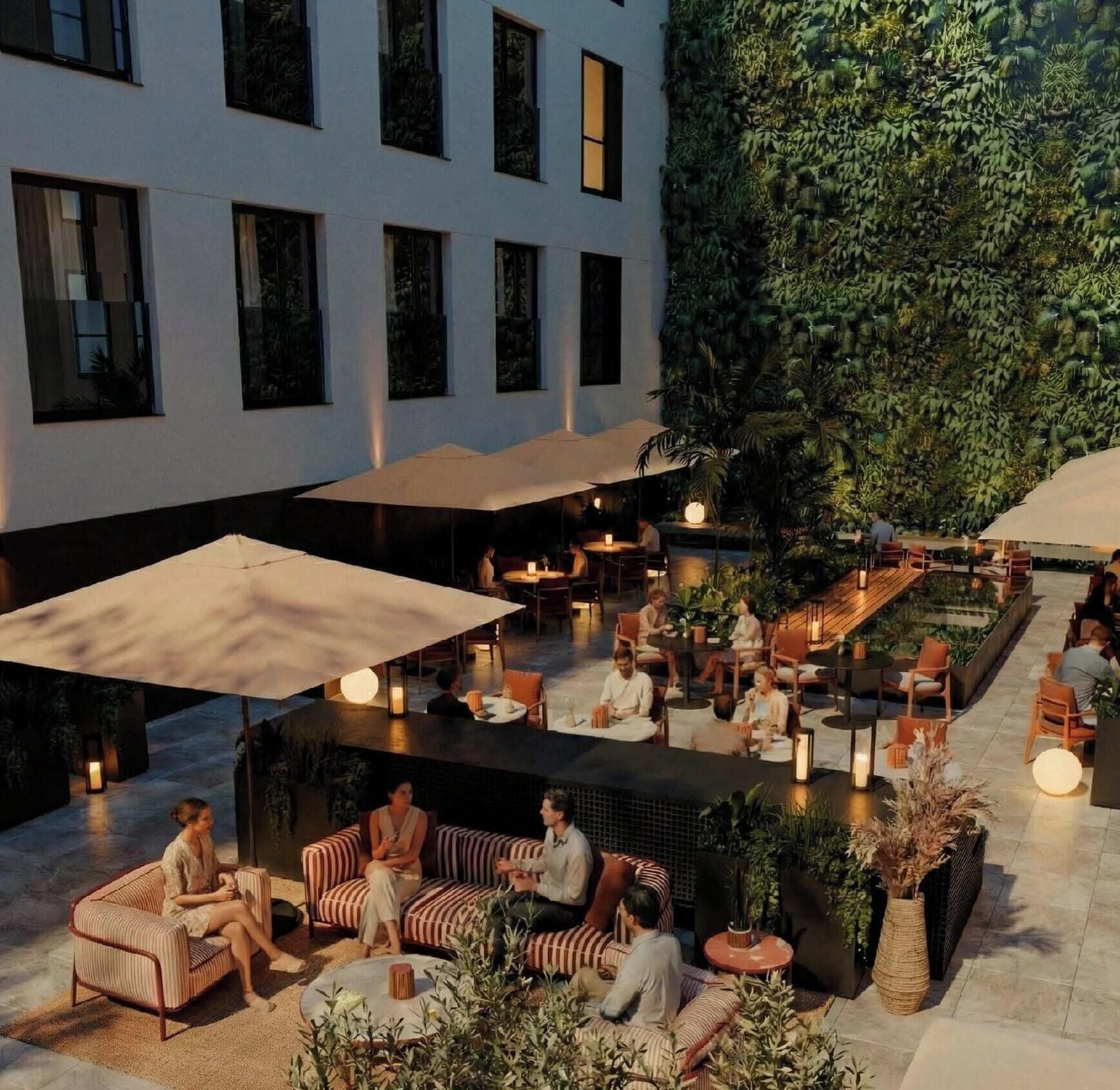 An outdoor seating area with tables and chairs, surrounded by greenery and a building with large windows.