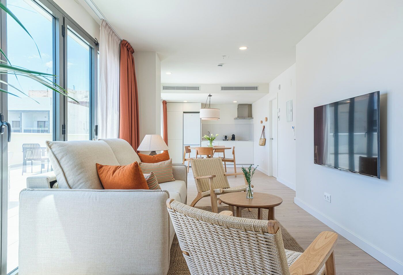 A modern living room with a sofa, chairs, a dining table, and a TV mounted on the wall.