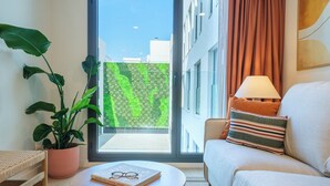 Un salón moderno con un sofá, una mesa redonda de madera, una planta en maceta y vistas a un jardín verde a través de un ventanal.
