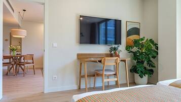Habitación de hotel con cama, escritorio y silla, televisor, planta y área de comedor con mesa y sillas.
