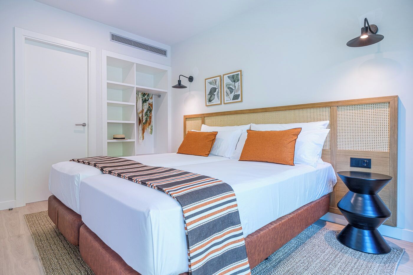 Une chambre d’hôtel avec un lit, une table de chevet, une lampe fixée au mur et une porte donnant sur un placard.