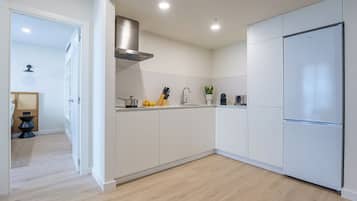 Una cocina moderna con armarios blancos, una campana extractora de acero inoxidable y un refrigerador empotrado.