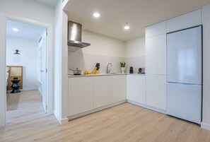 Una cocina moderna con armarios blancos, una campana extractora de acero inoxidable y un refrigerador empotrado.