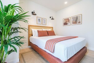 Un dormitorio con cama, una planta grande en maceta e iluminación en la pared.