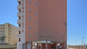 A multi-story building with 'BUENA VISTA' written on the facade, a parking area with cars, and a palm tree symbol. - Buena Vista 304 (Gulf Shores)