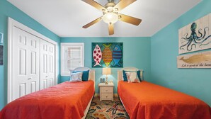 A bedroom with two beds, a ceiling fan, a wall with fish-themed artwork, and a door. - Buena Vista 304 (Gulf Shores)