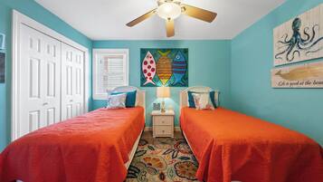 A bedroom with two beds, a ceiling fan, a wall with fish-themed artwork, and a door.