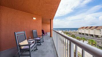 A balcony with rocking chairs and a view of the beach and hotel buildings.