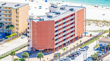 A multi-story hotel with a red facade, a parking lot, and a beach in the background.