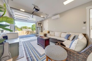 Una sala de estar moderna con un sofá, una mesita redonda pequeña, un escritorio con una silla y un ventanal grande.