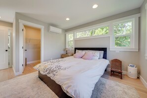 Un dormitorio con una cama grande, una silla de madera, una mesita de noche y una ventana con vistas a árboles.