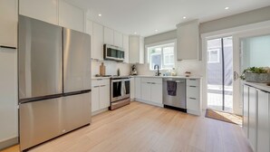 A modern kitchen with stainless steel appliances, white cabinetry, and a wooden floor. - Rooftop Deck + Private Patio! West Seattle Home (Seattle)