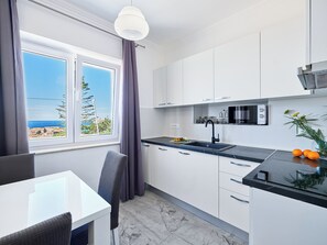 Una cocina moderna con armarios blancos, encimera negra y vistas al mar.