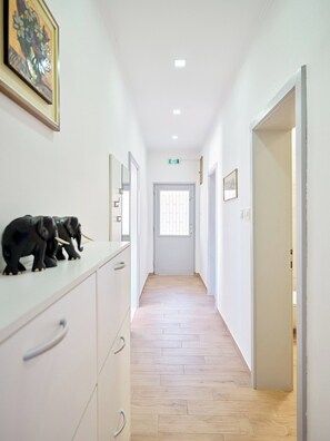 Un pasillo con pared blanca, suelo de madera y una puerta al final.