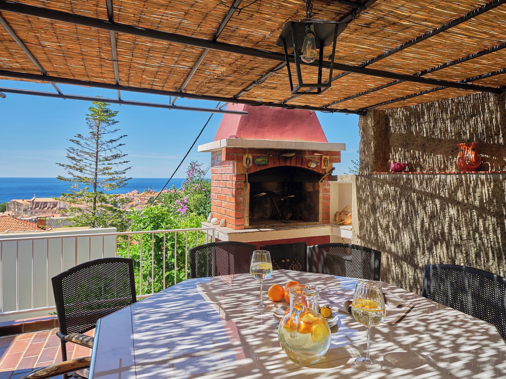 An outdoor dining area with a brick oven, table with chairs, and a view of the sea.