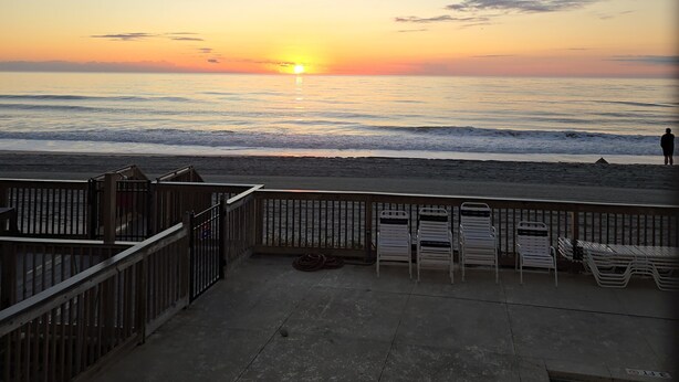 A beach view with a sunset, a pool, and a wooden deck with chairs. - 2-bedroom Oceanfront condo in peaceful Murrells Inlet with AC comfort (Murrells Inlet)