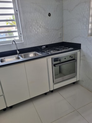 A kitchen with a sink, stove, and oven, white cabinets, and a window with blinds. - Enjoyable 1-bedroom apartment with AC in charming Willemstad (Willemstad)