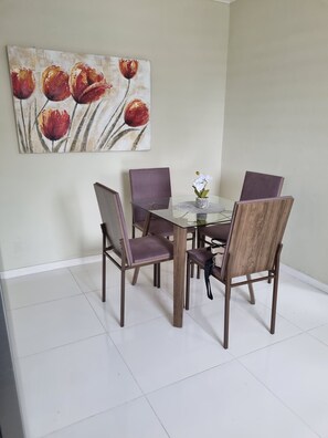 A dining area with a glass-top table, four wooden chairs, and a painting of tulips on the wall. - Enjoyable 1-bedroom apartment with AC in charming Willemstad (Willemstad)