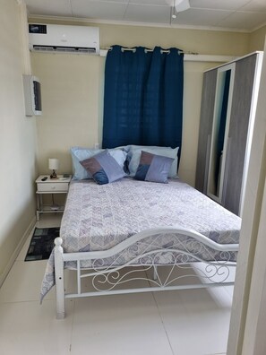 Ein Schlafzimmer mit Bett, Nachttisch, Klimaanlage, Spiegel und Vorhang.