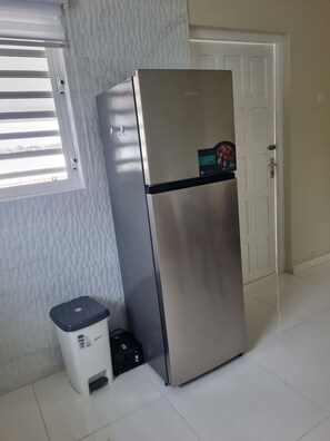Ein Edelstahl-Kühlschrank in einem Raum mit Fliesenboden und einer weißen Tür im Hintergrund.