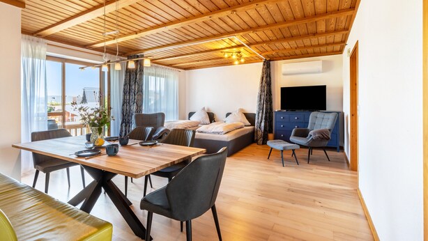 A modern interior with a wooden ceiling, a dining area, a sofa, and a TV.