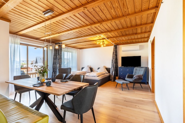 A modern interior with a wooden ceiling, a dining area, a sofa, and a TV.