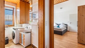A compact room with a washing machine, sink, and a bed with a view of the outdoors.
