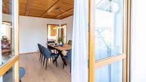 A dining area with a wooden table and chairs, a hanging light fixture, and a view through a glass door.
