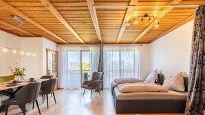 A modern room with a wooden ceiling, a bed, a desk with chairs, and a dining table.