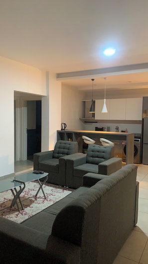 A modern living room with a sofa, a glass coffee table, and a kitchen area in the background. - Harmony Park Luxury Stay Near U.S. Embassy (Accra)