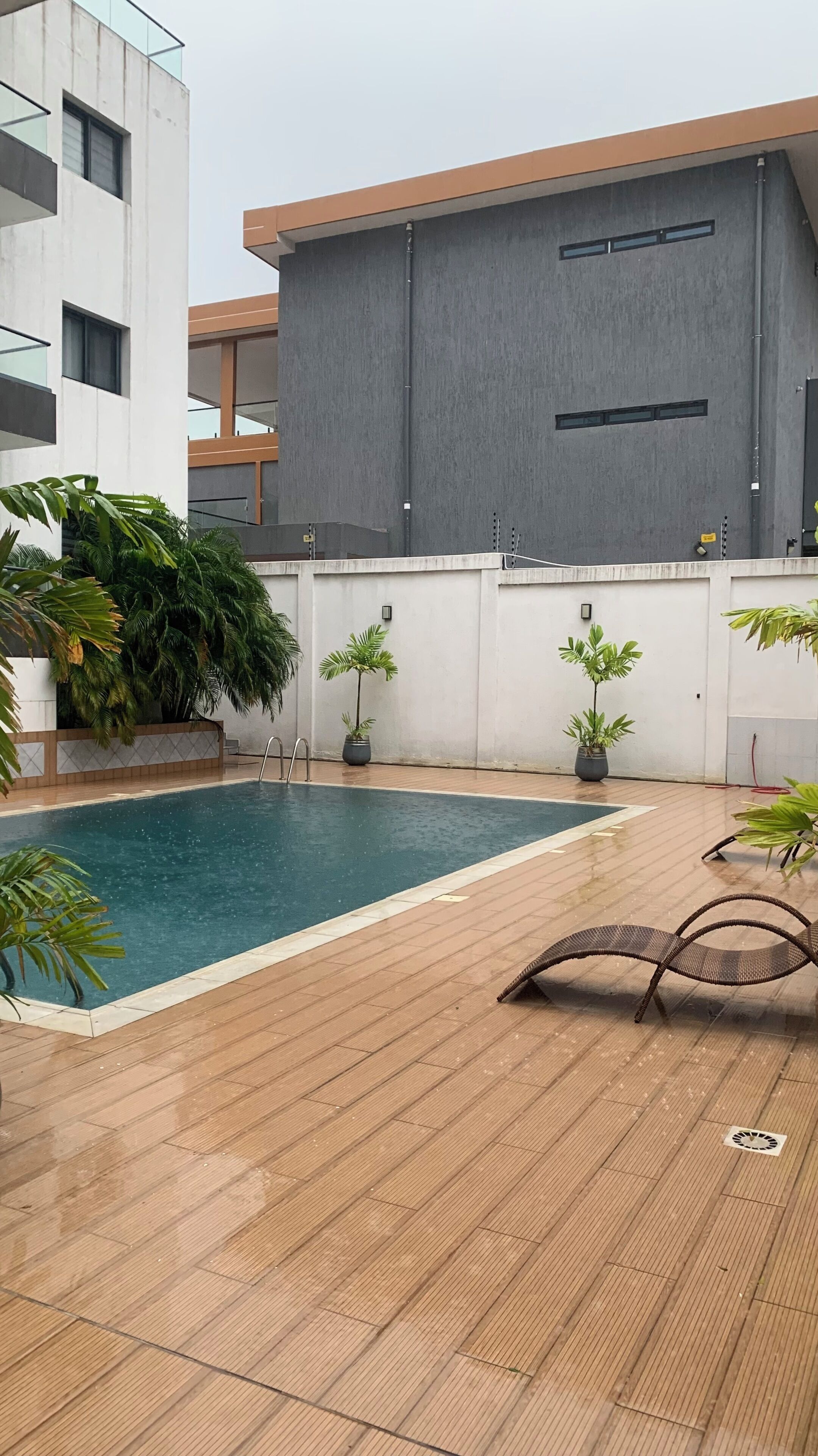 Ein Pool auf dem Dach mit einer Holzdachterrasse, Topfpflanzen und einem modernen Gebäude im Hintergrund.