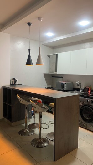 A modern kitchen with a central island, bar stools, a microwave, and a washing machine. - Harmony Park Luxury Stay Near U.S. Embassy (Accra)