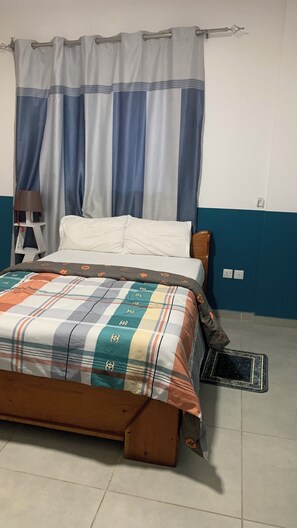 A bedroom with a bed, curtains, a nightstand, and a wall socket. - Harmony Park Luxury Stay Near U.S. Embassy (Accra)