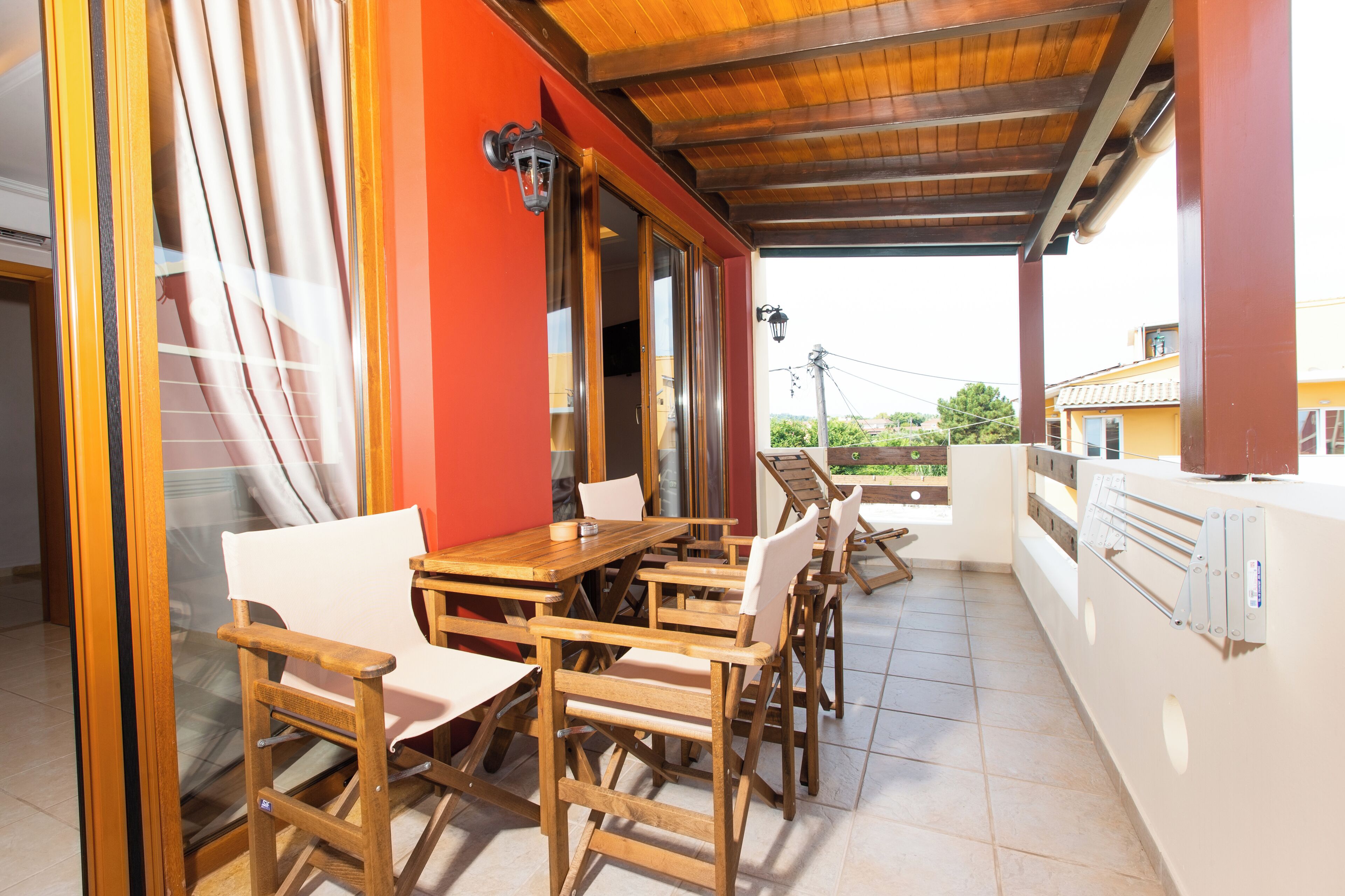 An outdoor patio with wooden furniture, a red wall, and a view of the surrounding area.