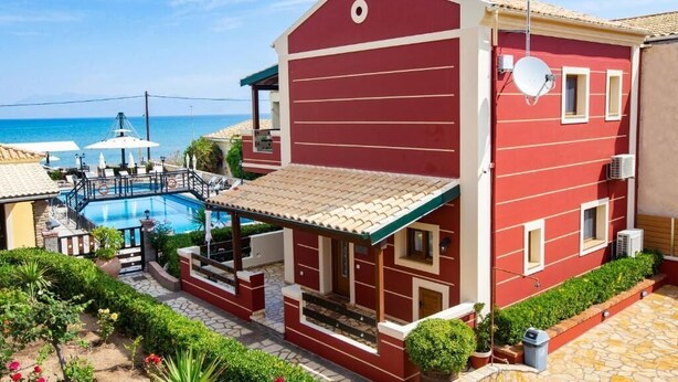 Um edifício vermelho com piscina, alpendre coberto e vista para o mar.